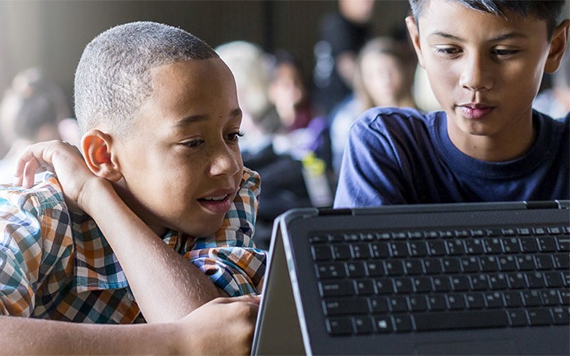 Two young students working on a HP device